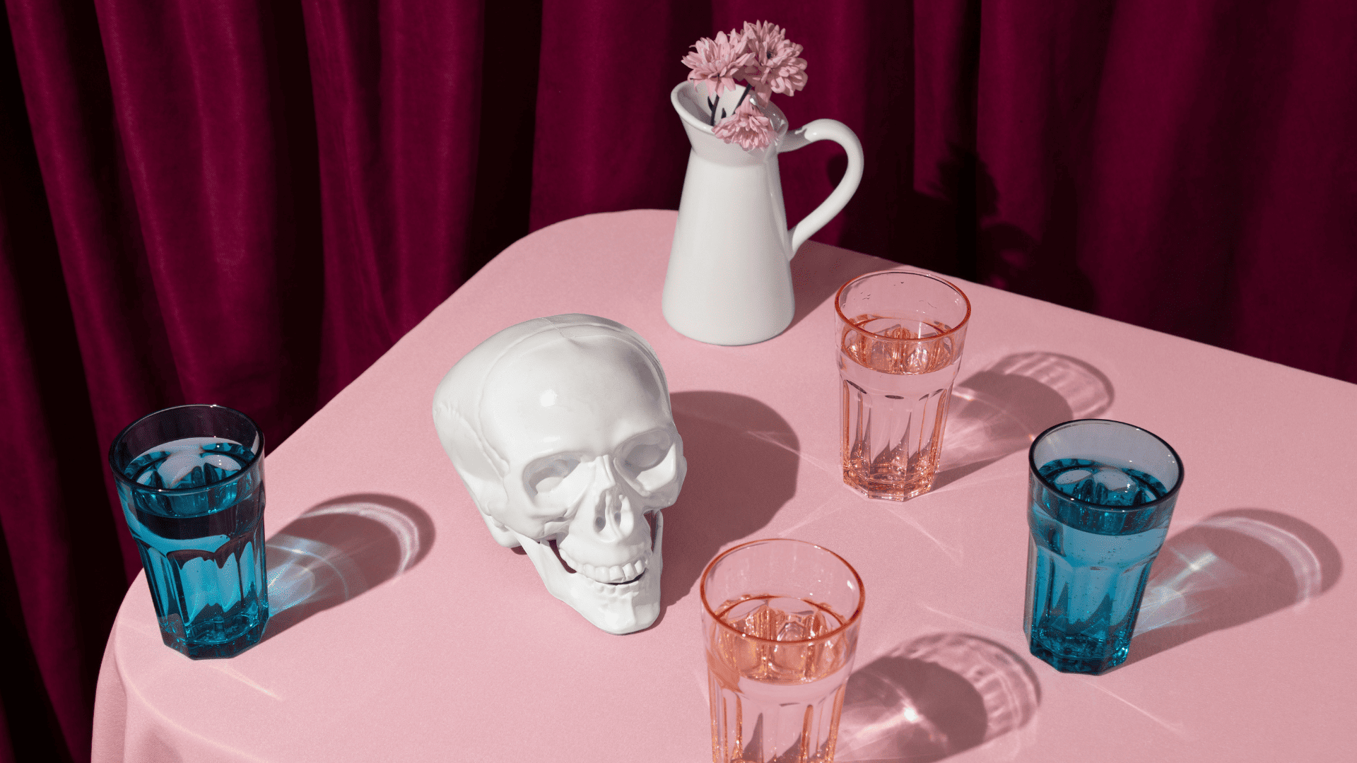 calavera cerámica y vasos facetados sobre tela rosa