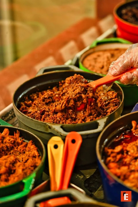 gloved hand scooping shredded meat from buffet pans