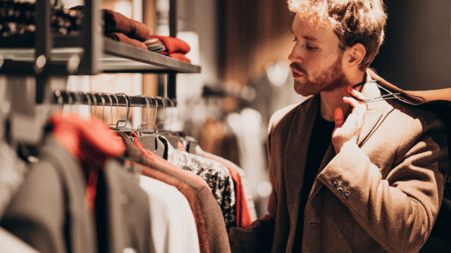 hombre elegante elige abrigo en boutique cálida