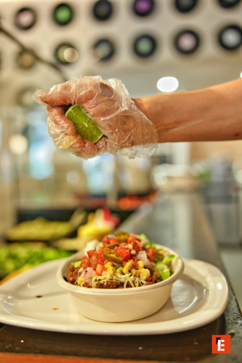 gloved hand squeezing lime over colourful salad bowl