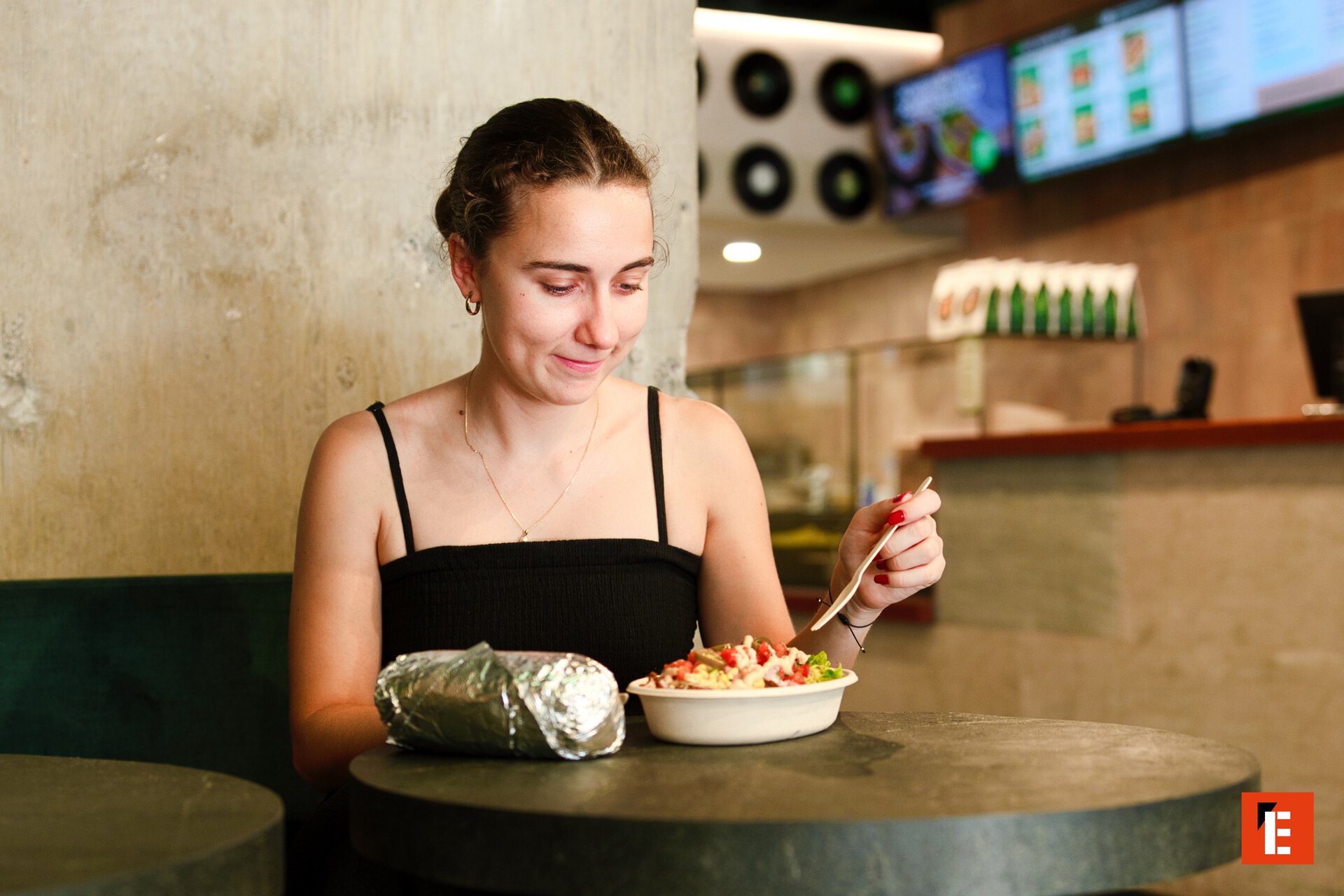 young woman eating burrito and salad bowl