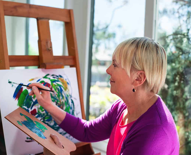 woman painting colourful abstract by window