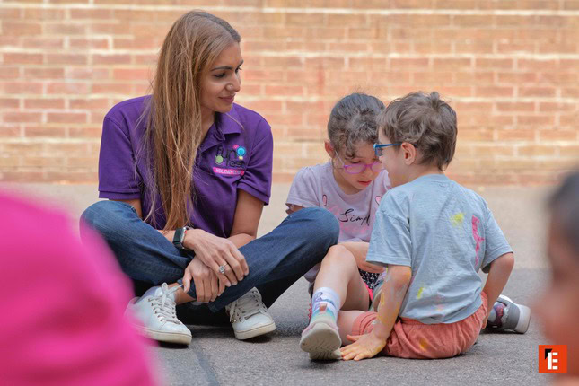 caregiver guiding children outdoors by brick wall