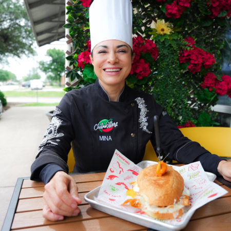 chef mina sonríe con sándwich gourmet al aire libre