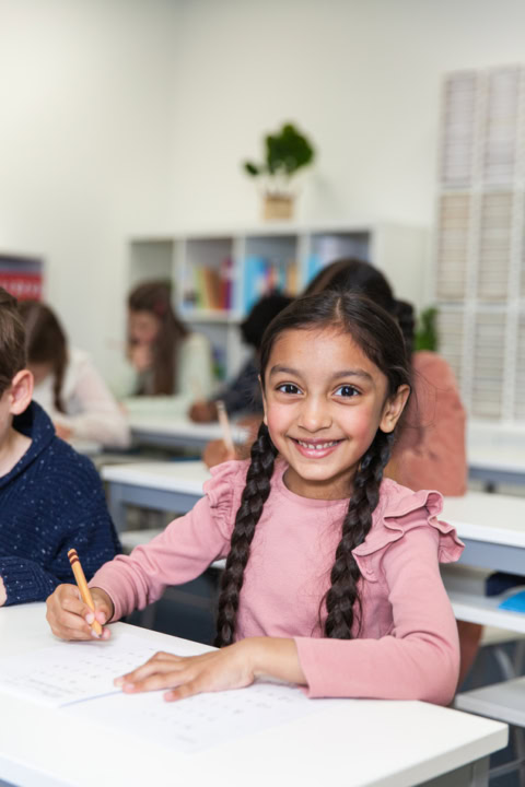 Écolière souriante en classe avec cahier et crayon