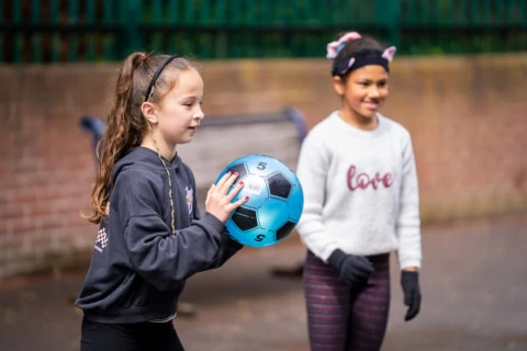 two girls playing with blue football on playground