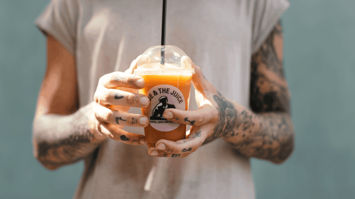 mains tatouées tenant un jus orange frais Joe & The Juice