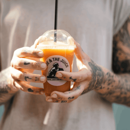 mains tatouées tenant un jus orange frais Joe & The Juice
