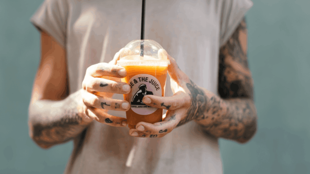 mains tatouées tenant un jus orange frais Joe & The Juice
