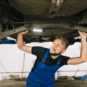 mecánico inspecciona suspensión de coche elevado en taller