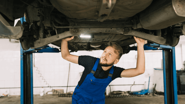 mecánico inspecciona suspensión de coche elevado en taller