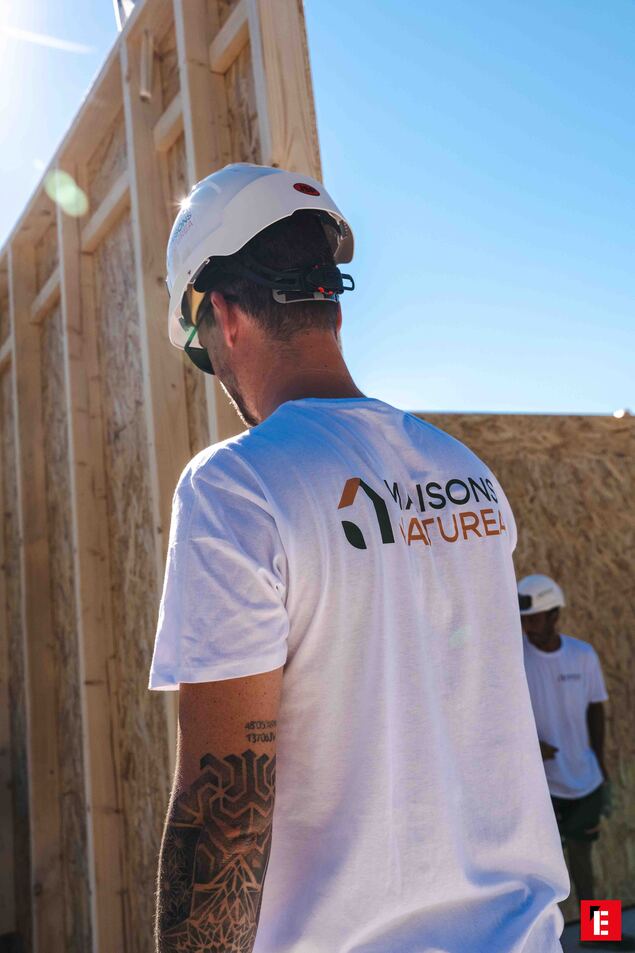 ouvrier casqué sur chantier ossature bois ensoleillé, bras tatoué