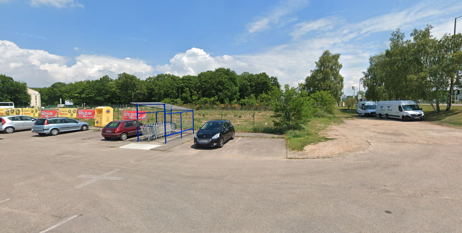 parking ensoleillé avec abri à chariots et lisière boisée