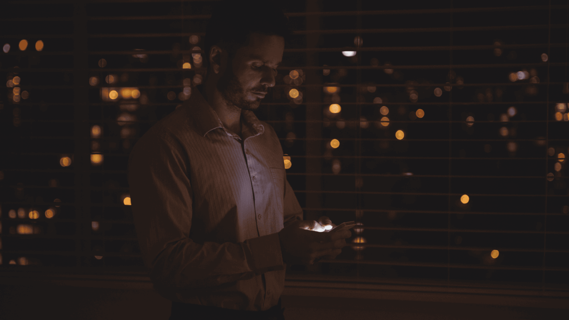 hombre con móvil junto a ventana nocturna