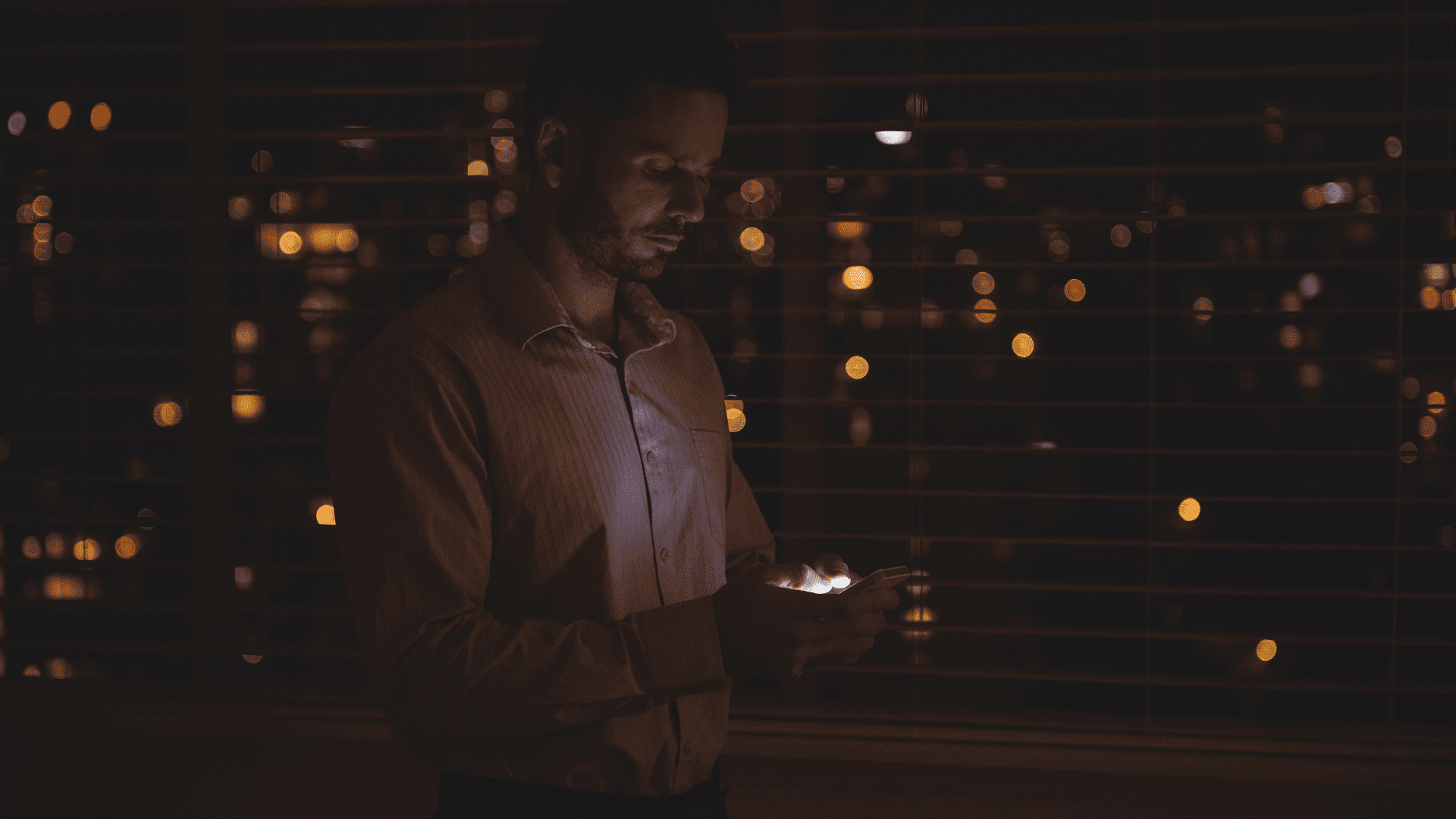 hombre con móvil junto a ventana nocturna