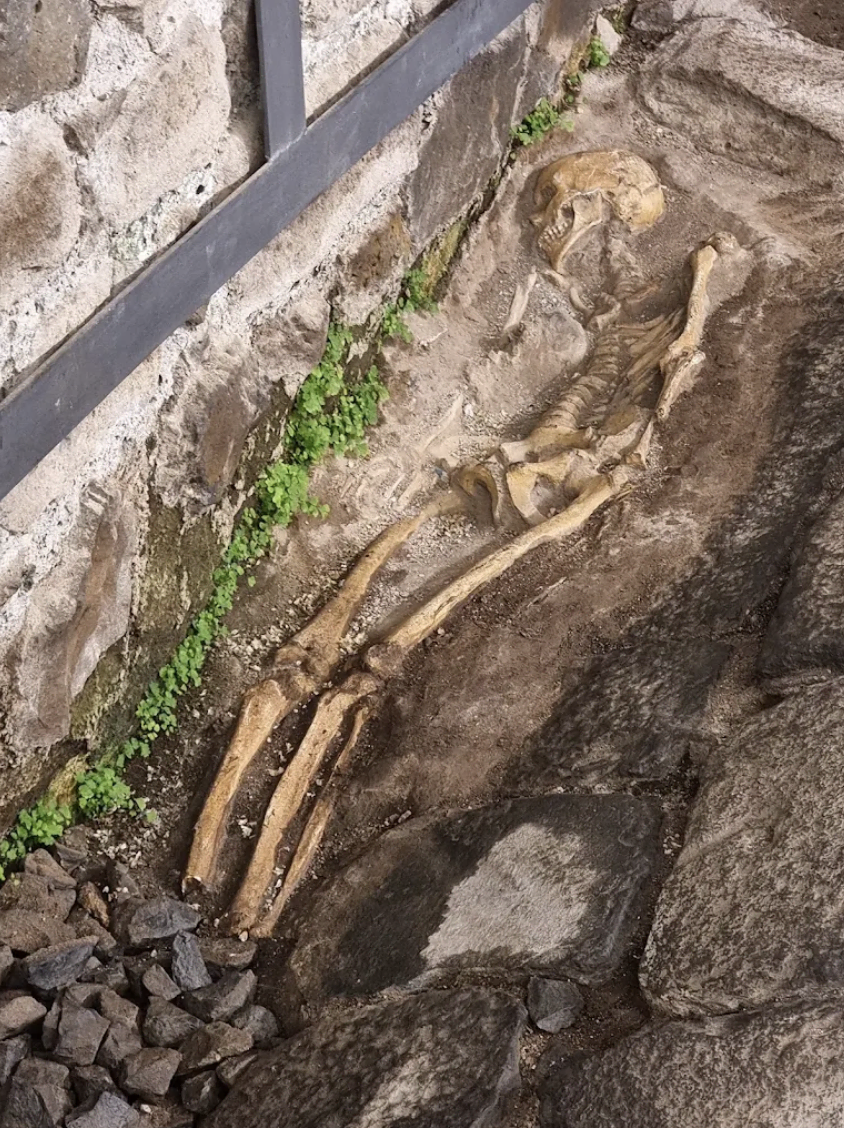 scheletro antico in scavo tra pietre e muro