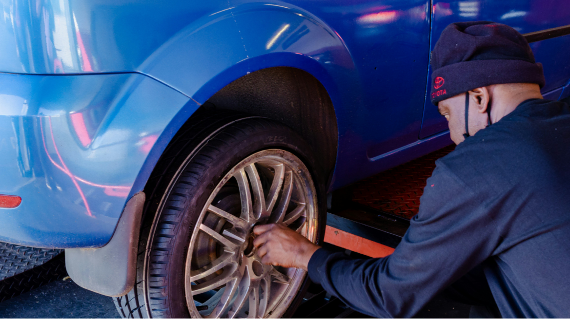 mechaniker prüft rad am blauen auto in der werkstatt