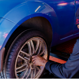 mechaniker prüft rad am blauen auto in der werkstatt