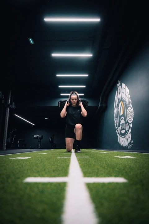 entraînement femme au sandbag sur turf indoor