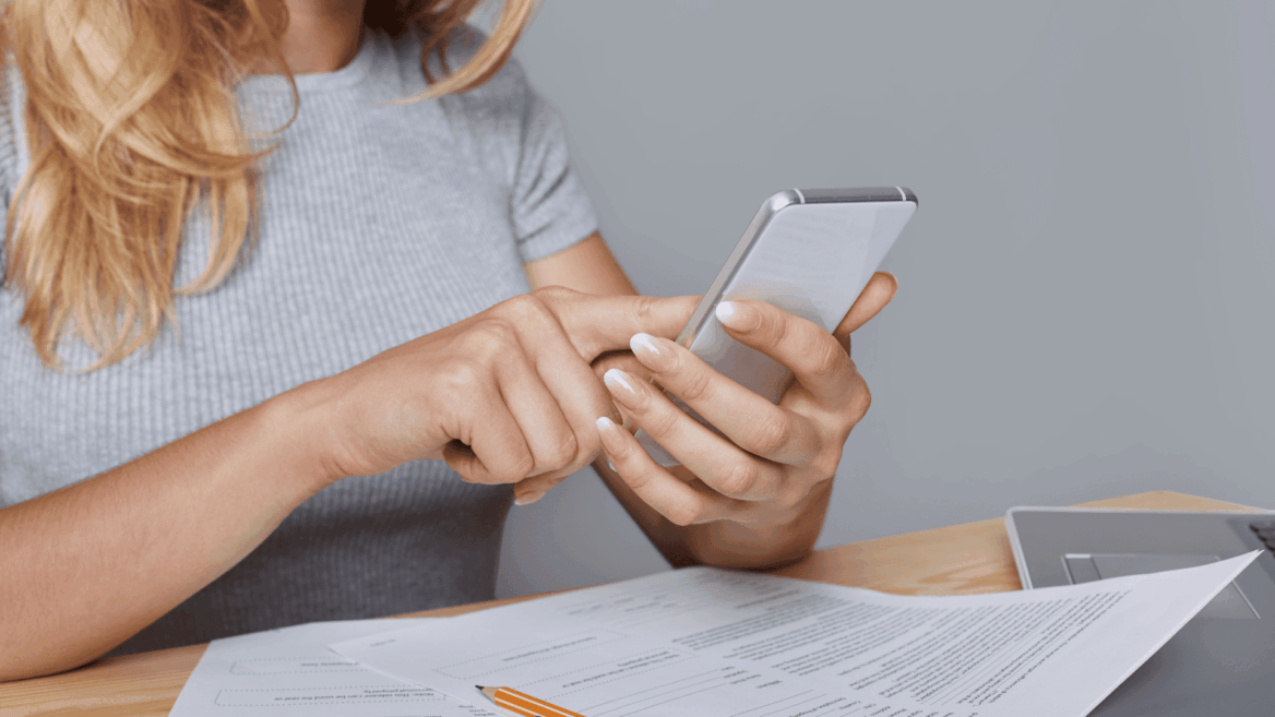 mujer concentrada con móvil, documentos y portátil
