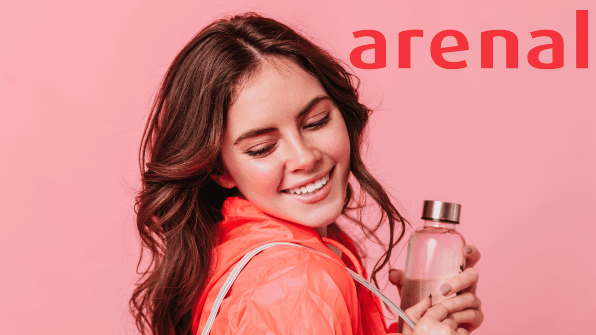 mujer sonriente con chaqueta coral y botella perfume rosa
