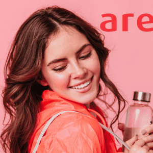 mujer sonriente con chaqueta coral y botella perfume rosa