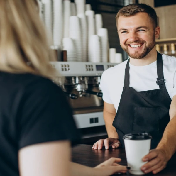 friendly café barista handing coffee to customer