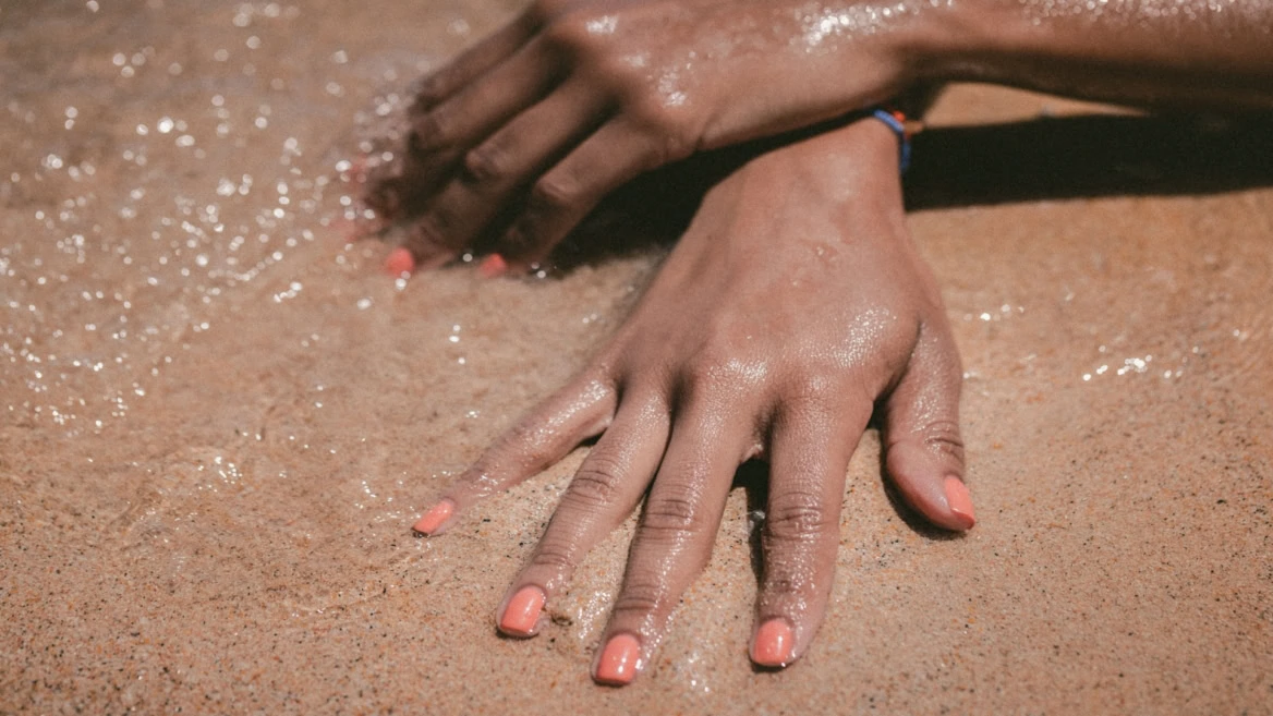 mains sur sable mouillé, vernis corail au bord de mer