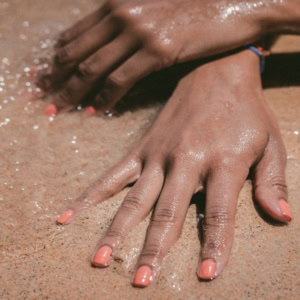 mains sur sable mouillé, vernis corail au bord de mer