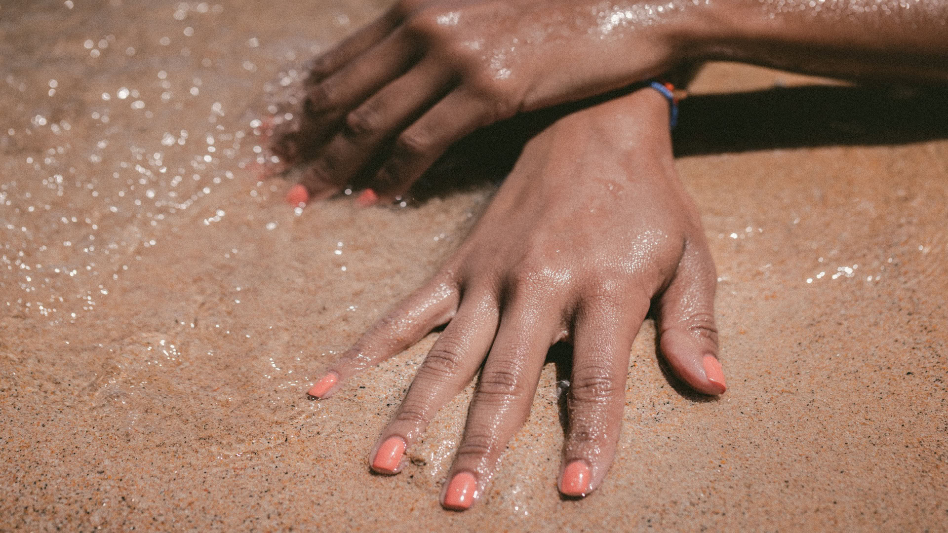 mains sur sable mouillé, vernis corail au bord de mer
