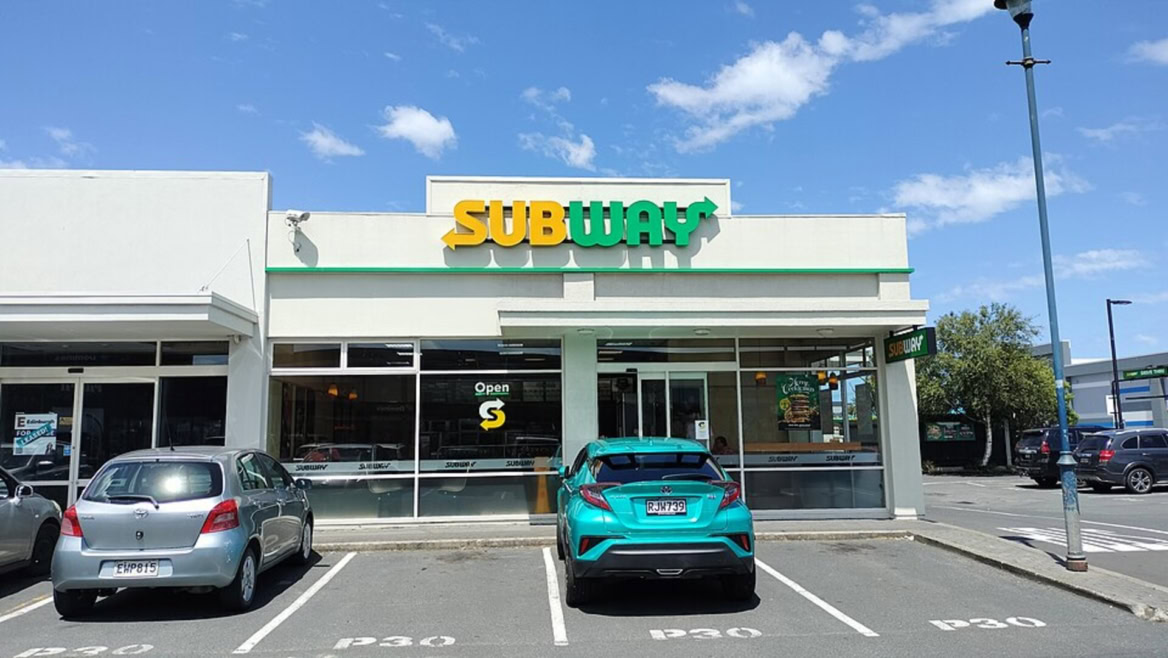 façade d’un subway au soleil, avec stationnement