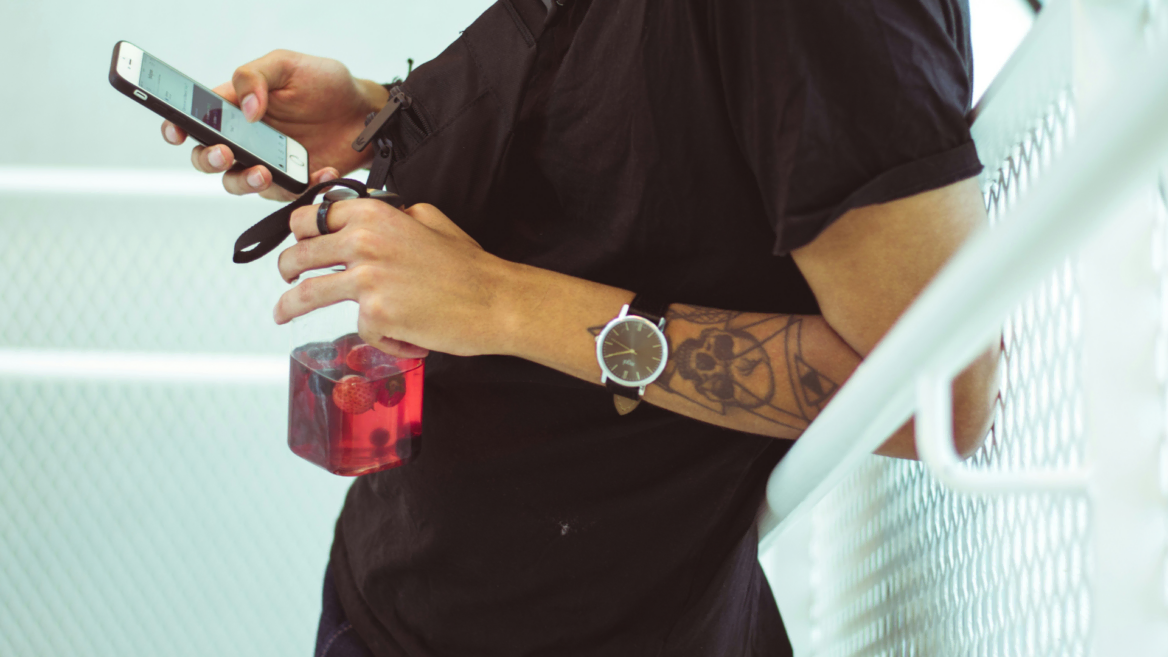 tattooed man with phone and red drink