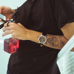 tattooed man with phone and red drink