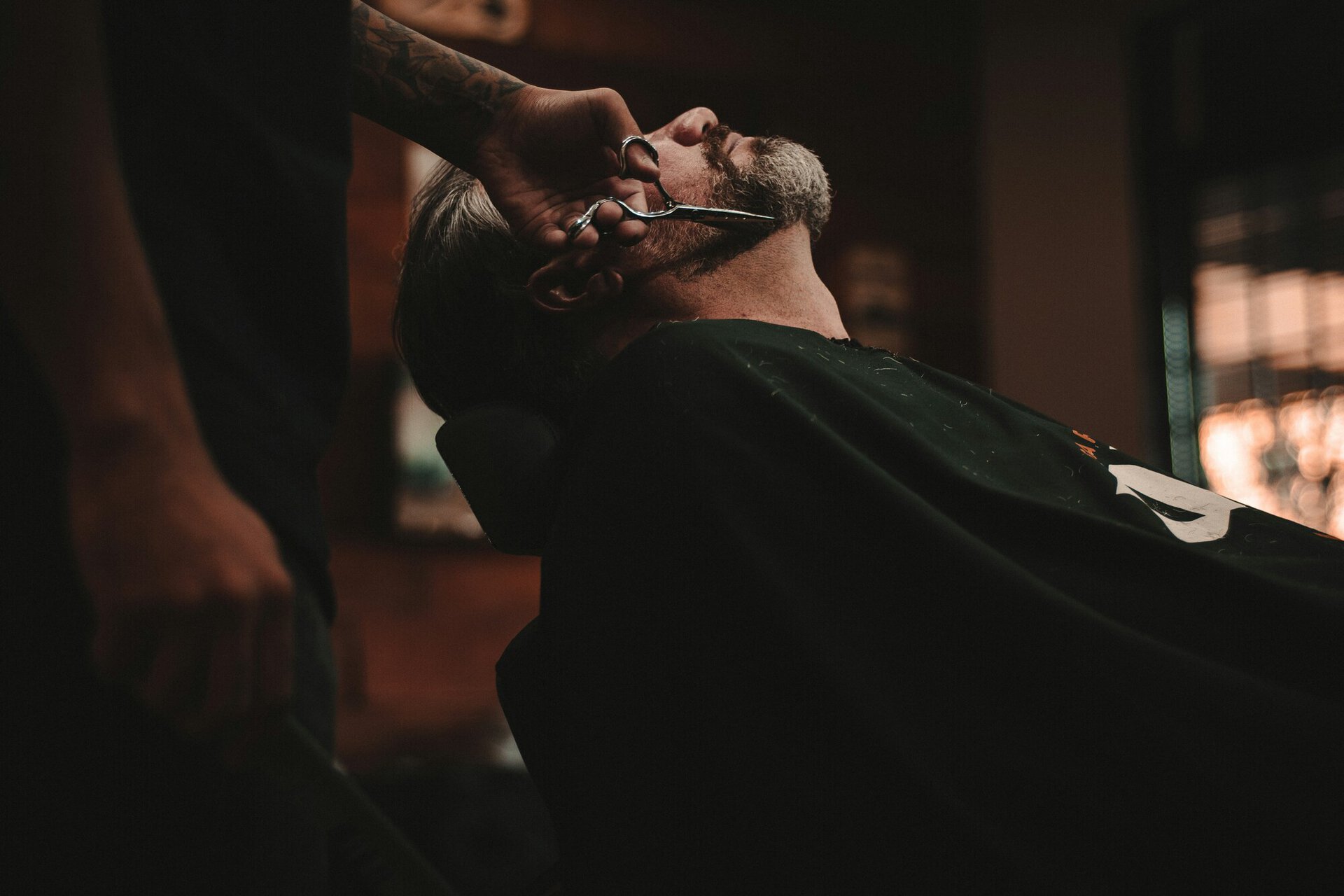 barber trimming grey beard in warm light