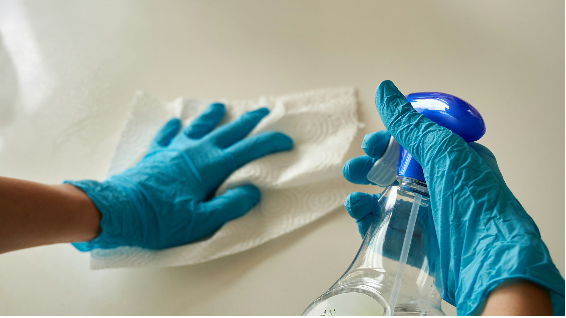 blue gloves cleaning surface with spray bottle