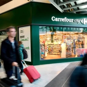 carrefour city en gare, passants flous et valise rose
