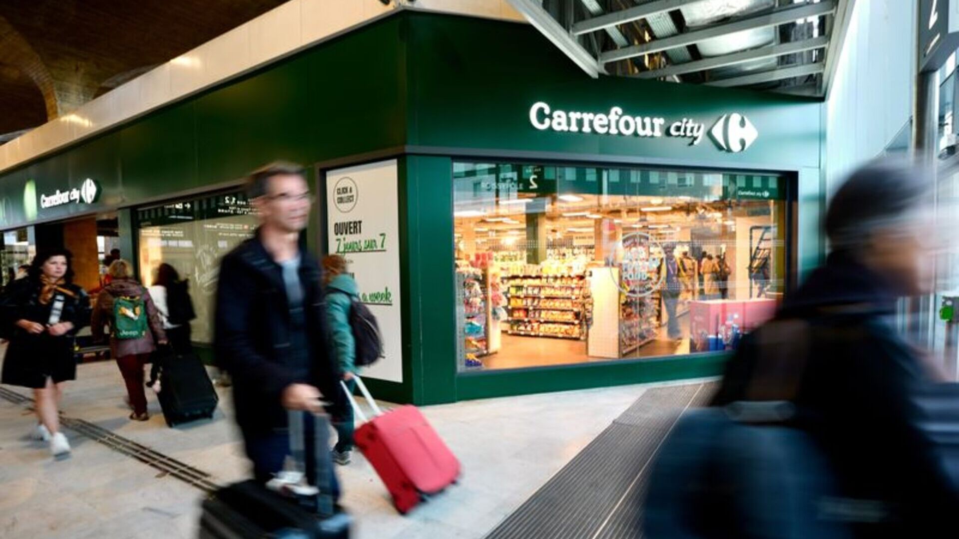 carrefour city en gare, passants flous et valise rose