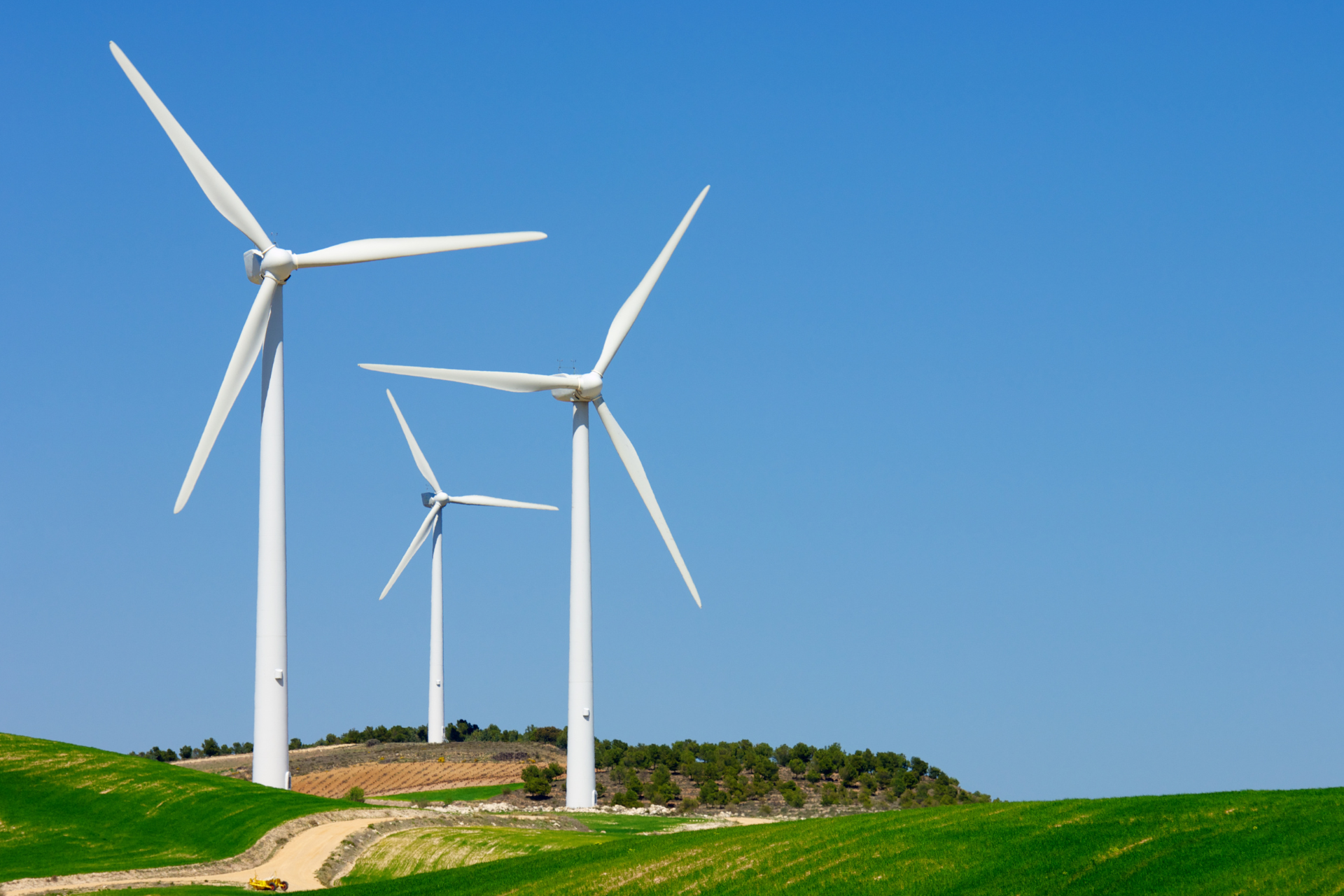 Éoliennes blanches sur colline verte, ciel bleu