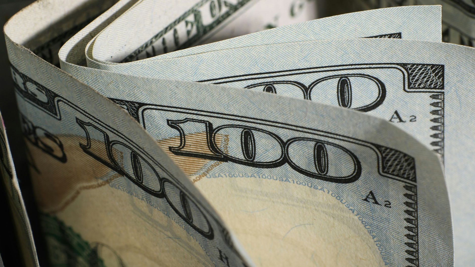 close up of folded $100 bills and blue security patterns