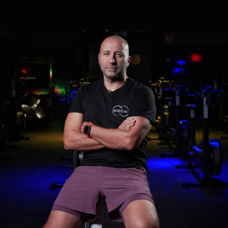 hombre en gimnasio con brazos cruzados y luces de neón