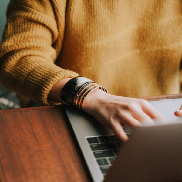 mains tapant sur laptop, pull jaune au bureau