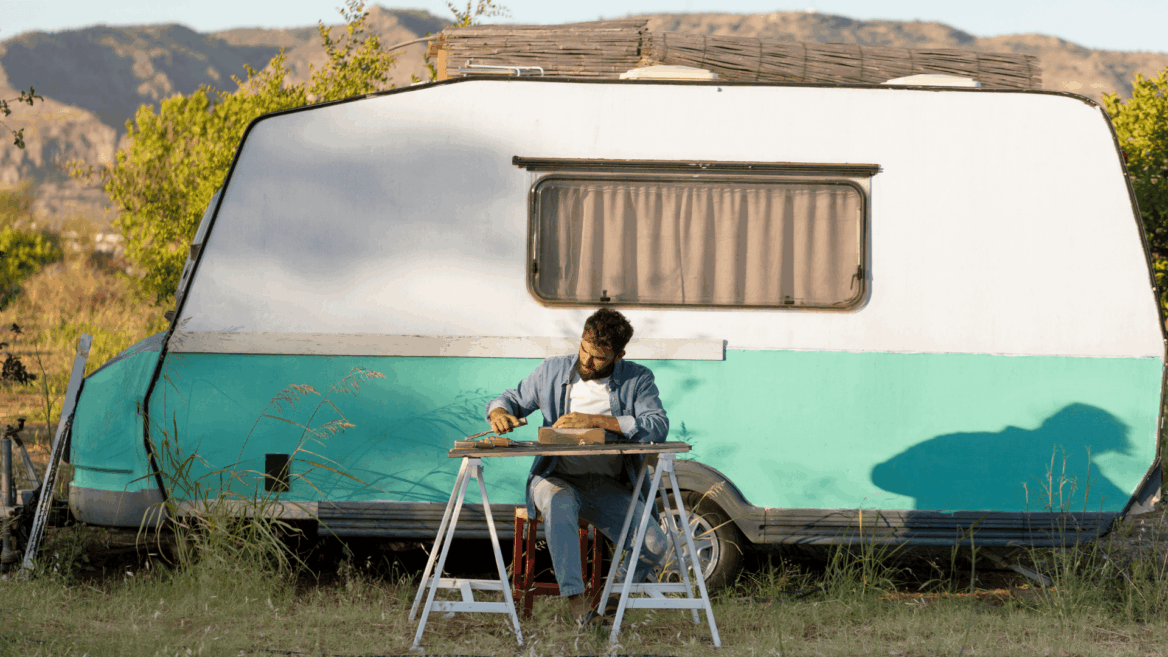 hombre trabajando junto a caravana vintage en el campo