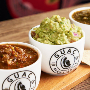 mexican salsa and guacamole cups on wood board