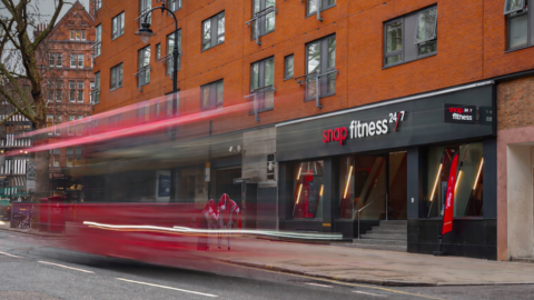 blurred red bus past snap fitness 24/7 storefront